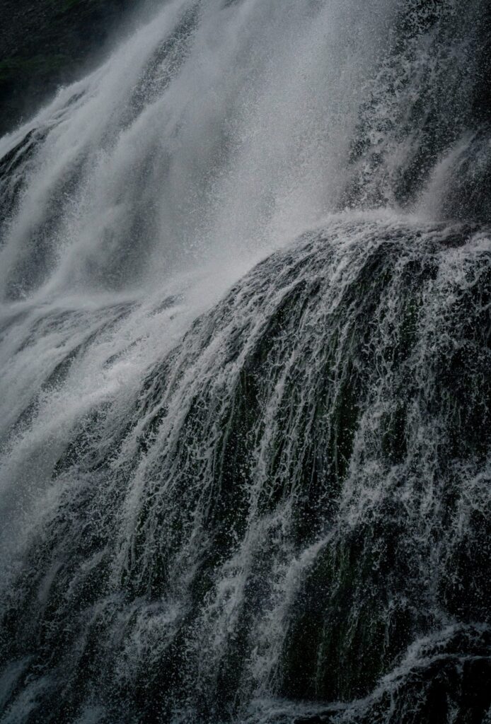 Nahaufnahme stürzenden Wassers an einem Wasserfall, Sprühnebel und dunkler Fels