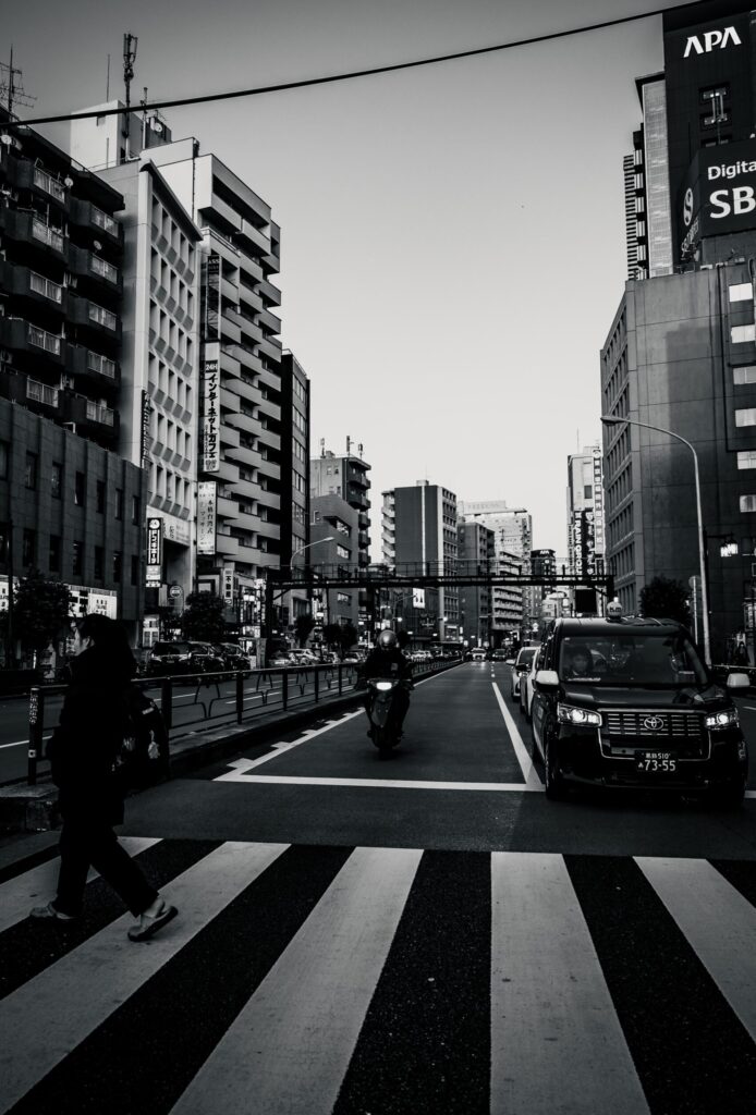 Straßenkreuzung in Japan, Schwarzweiß: Zebrastreifen, Taxi, Motorrad, Hochhäuser