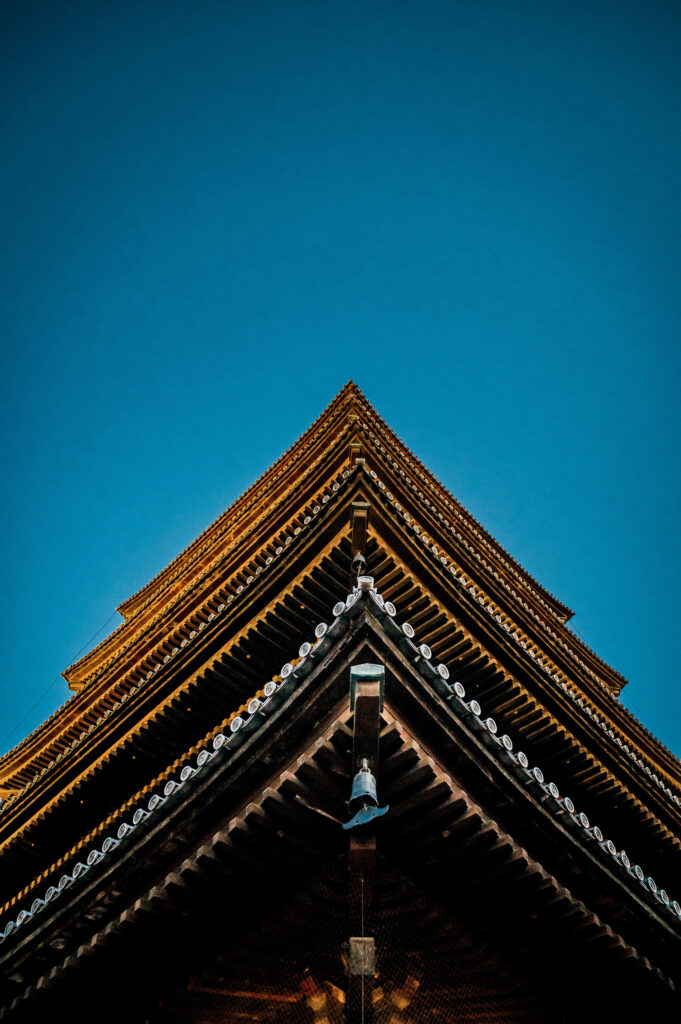 Unteransicht eines traditionellen japanischen Tempeldachs mit Giebel und Glocke vor blauem Himmel