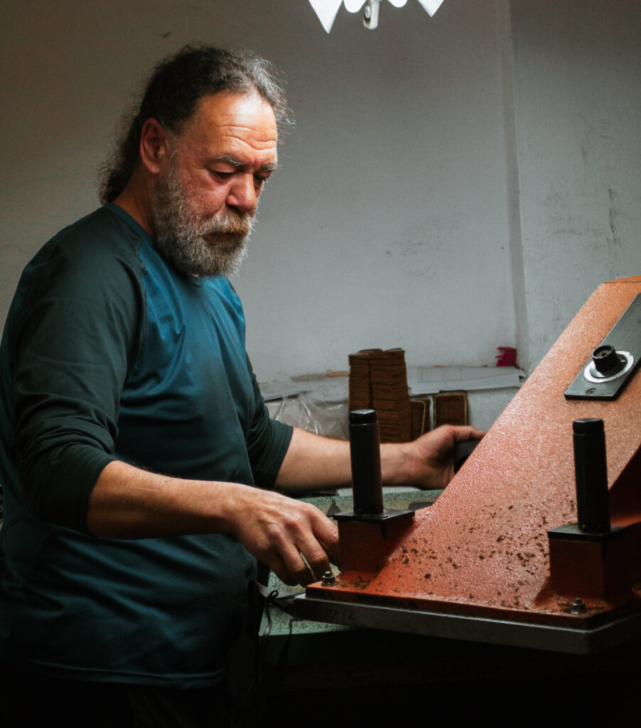 Handwerker mit Bart bedient orangefarbene Presse in der Panama-Jack-Schuhmanufaktur