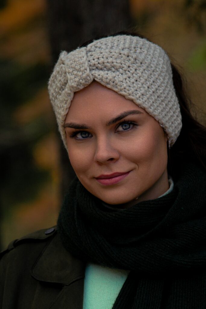 Junge Frau mit blauen Augen, cremefarbenem Strick-Stirnband und dunklem Schal, Portrait im herbstlichen Wald
