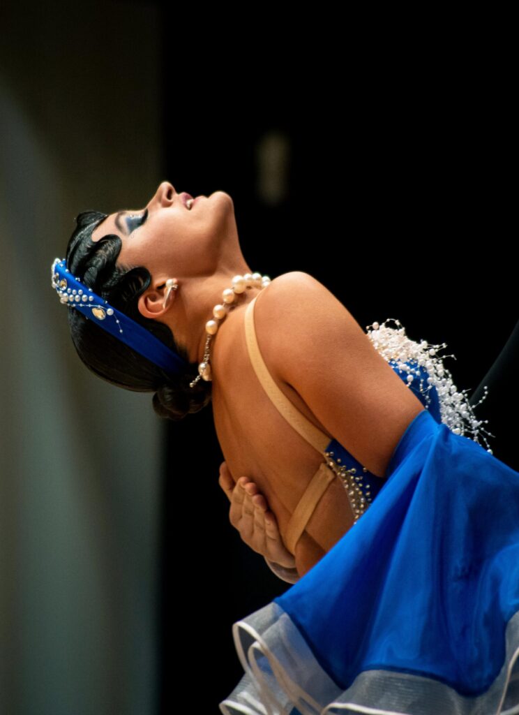 Tänzerin in blauem Kleid mit Perlen und blauem Haarband, Kopf nach hinten geneigt, dramatische Pose