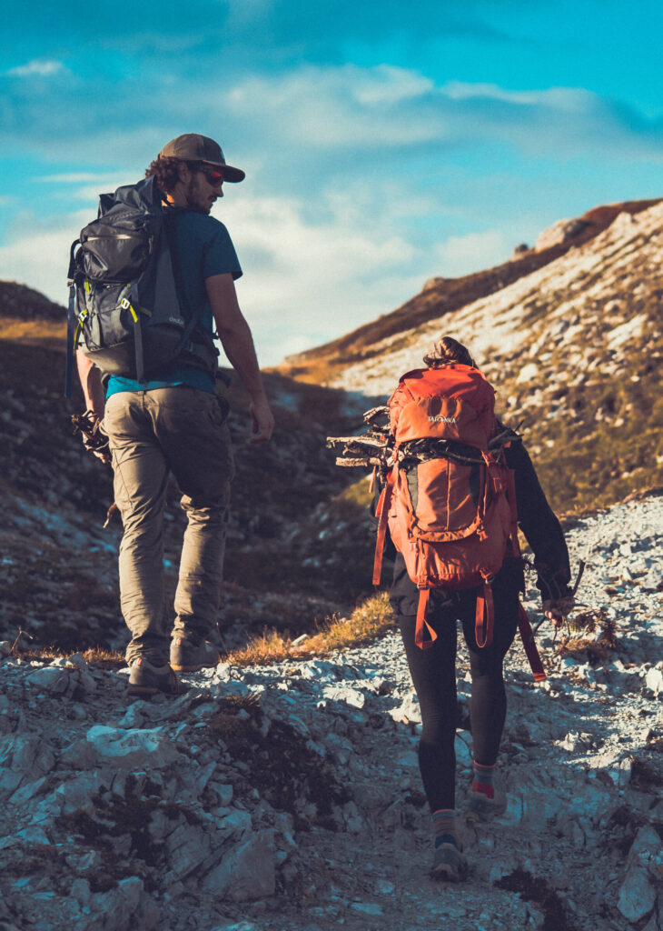 Zwei Wanderer mit Rucksäcken auf steinigem Bergpfad in den Tiroler Alpen